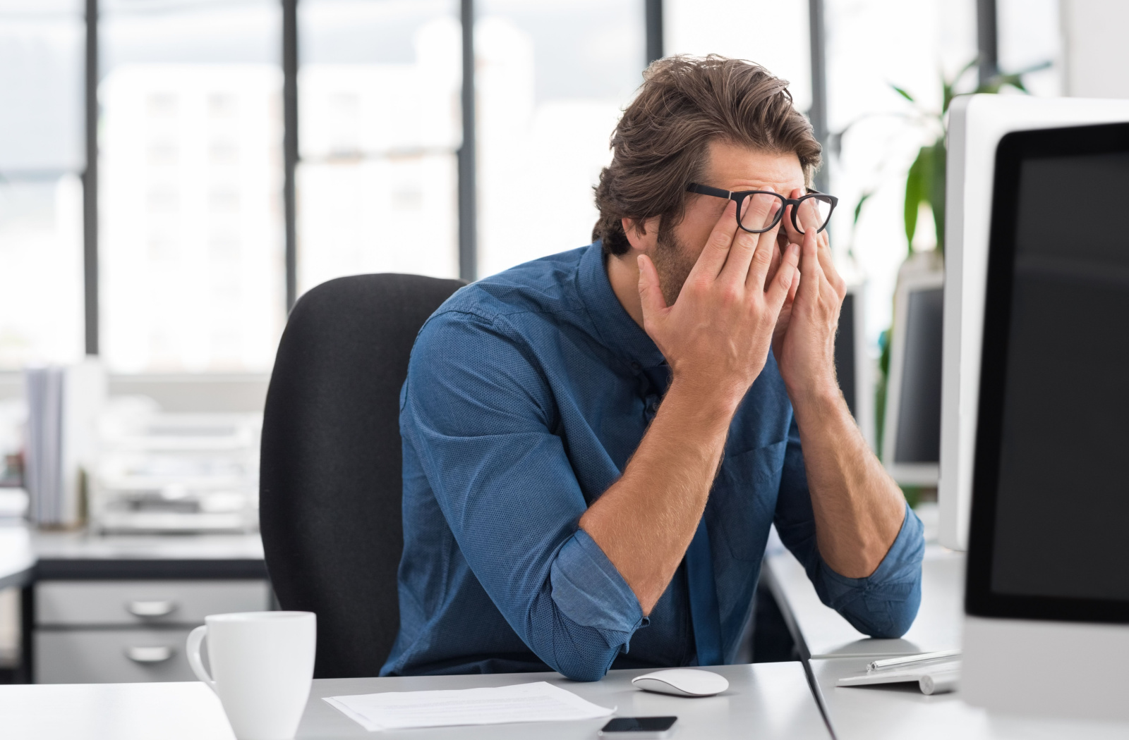 A professional-looking man rubbing both of his eyes because of eye strain.